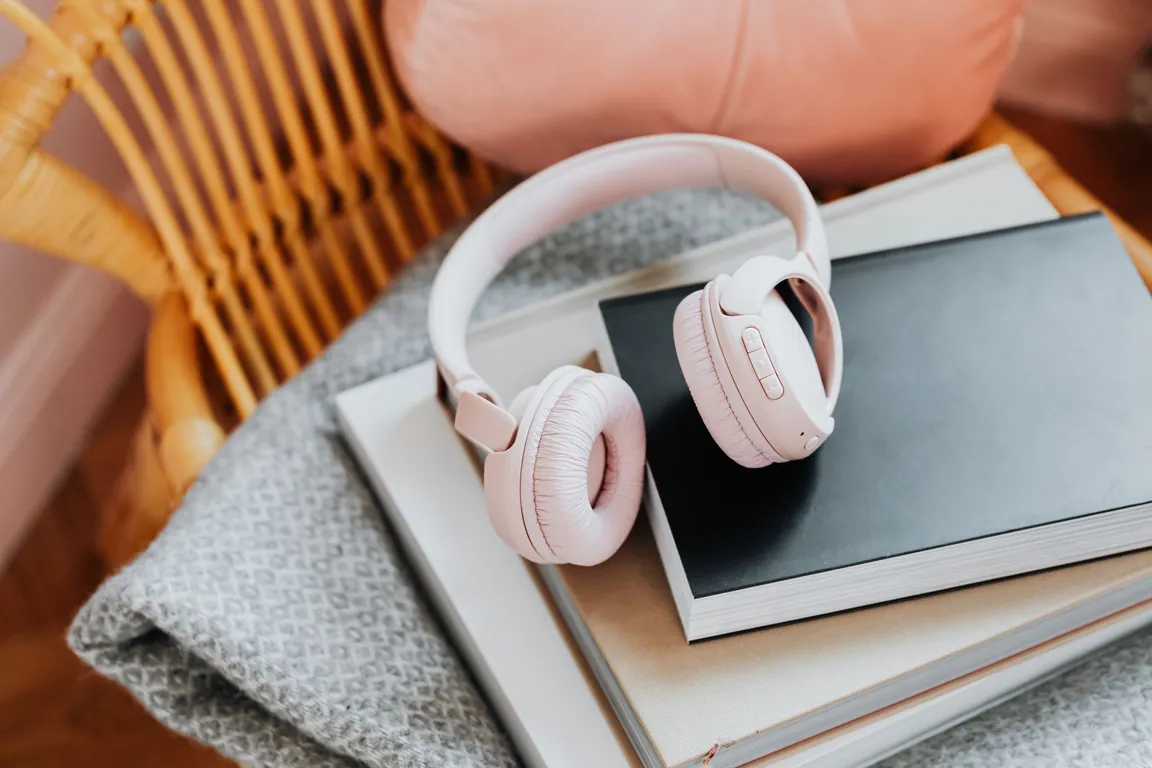 Pink headphones on a stack of books in a cozy wicker chair, set up for an audiobook
