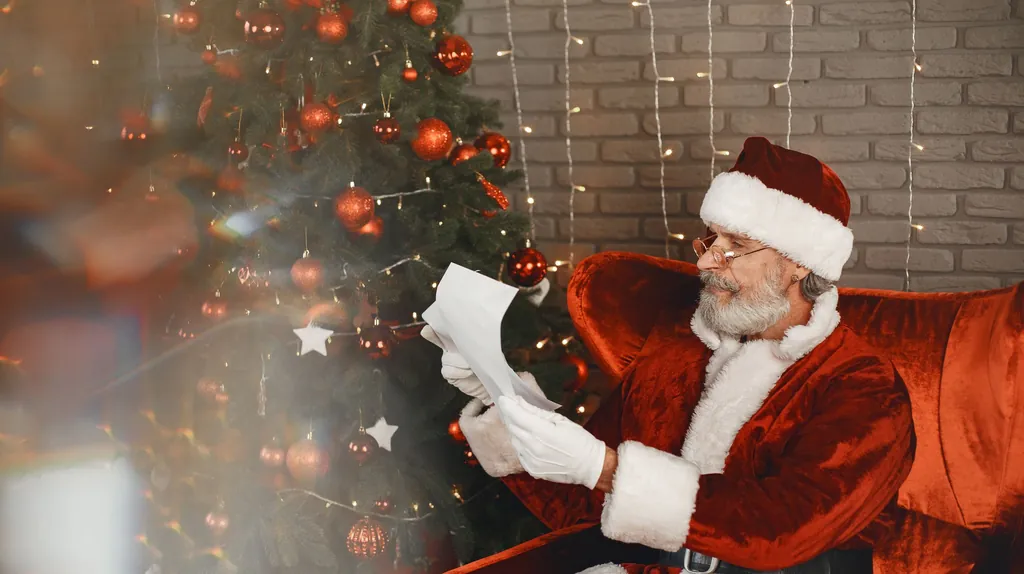 Santa Claus in a red armchair by the Christmas tree, reading a letter