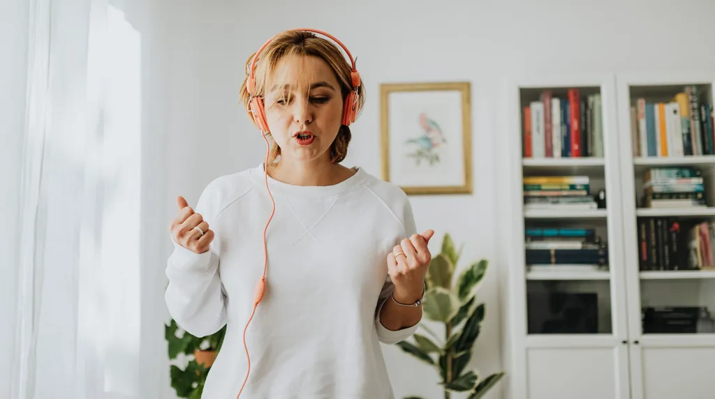 Woman in orange headphones singing along at home during a singing test