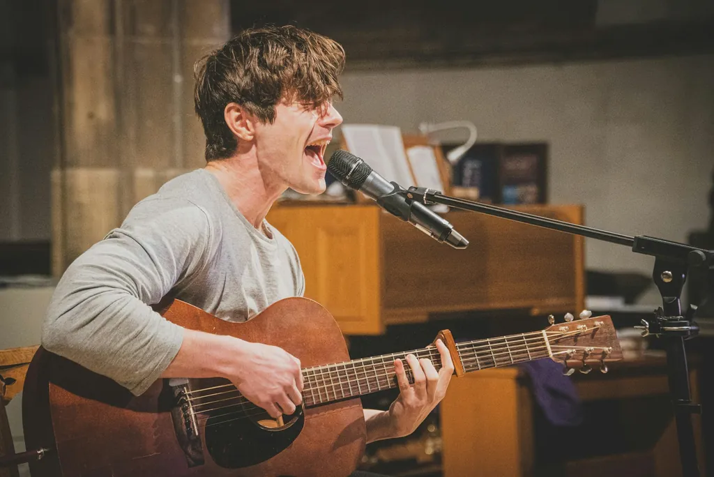 Young man playing an acoustic guitar and singing into a studio microphone