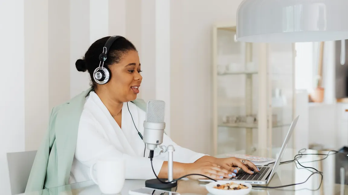 Woman in headphones at her desk with a USB microphone and a laptop, recording at home