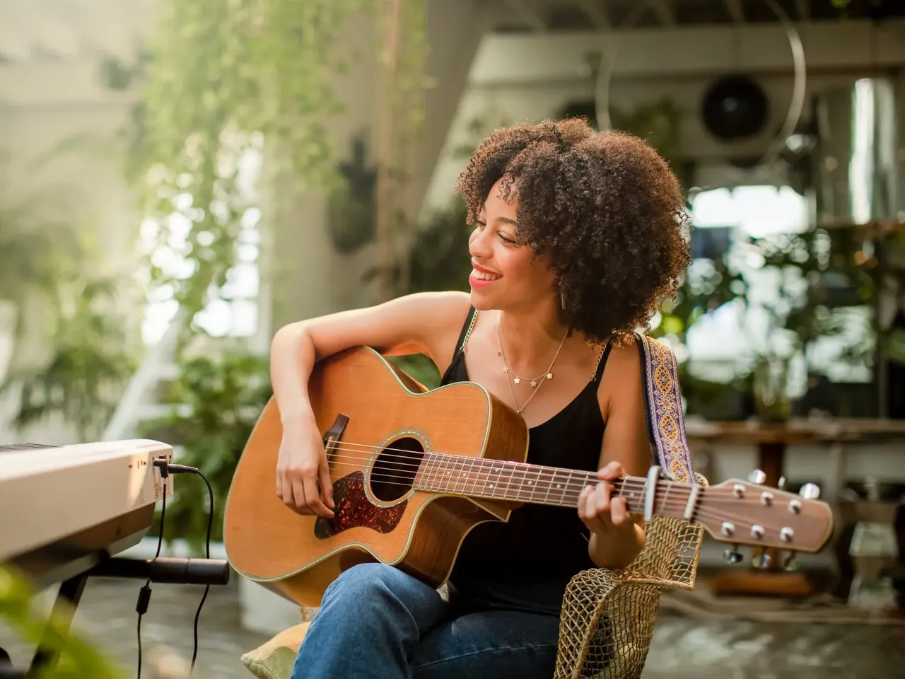 Smiling woman playing an acoustic guitar and singing in a sunny living room full of plants