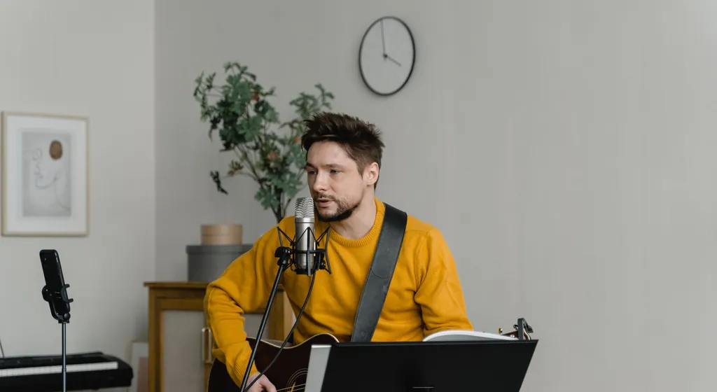 Young man with a guitar singing a song line into a microphone at home