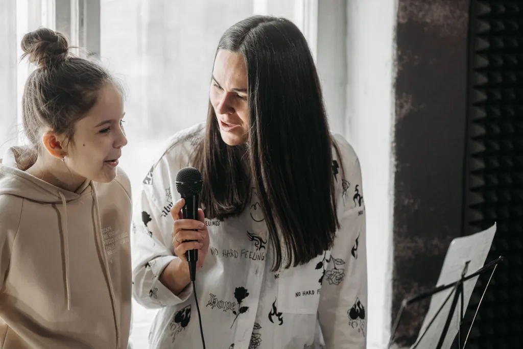 Voice teacher and a girl singing together during a warm-up, the girl holding a microphone