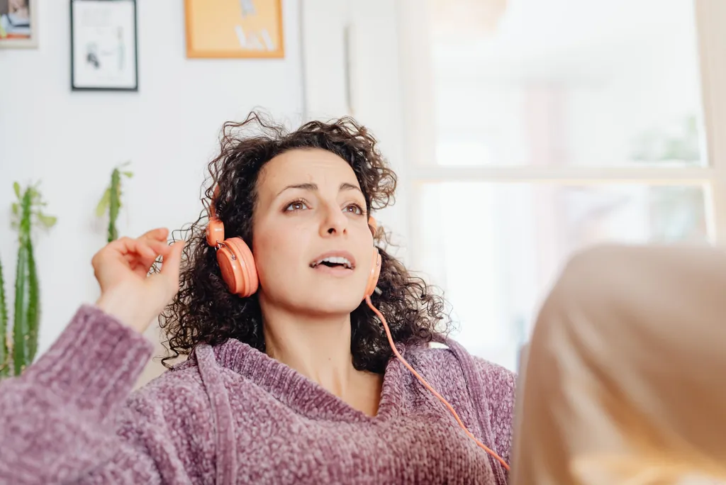 Woman in orange headphones singing at home, practicing before her next AI singing score