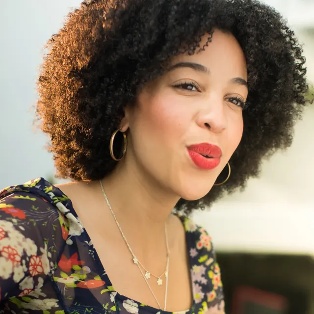 Curly-haired woman with red lipstick singing a low, warm note