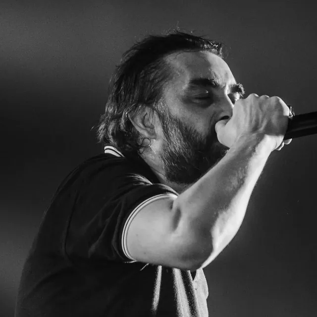 Bearded singer belting into a microphone, in a rose-tinted black-and-white photo