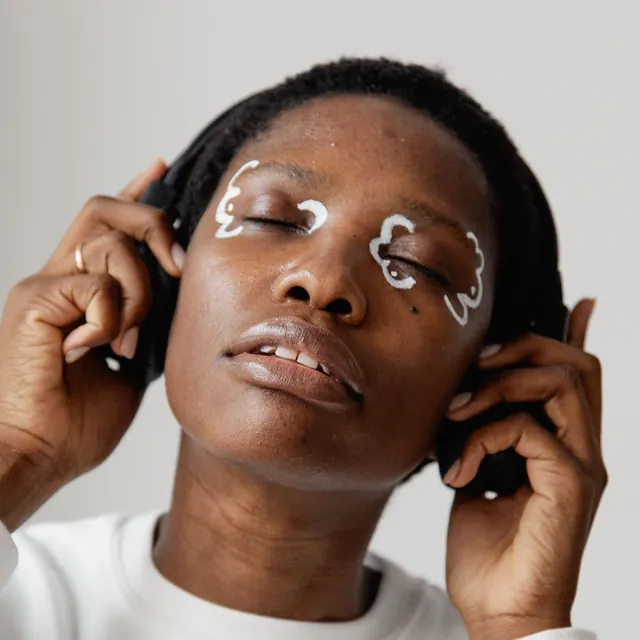 Woman with white graphic eyeliner holding her headphones and listening with her eyes closed
