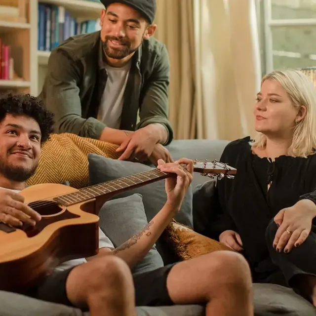 Friends on a sofa singing along while one plays the guitar