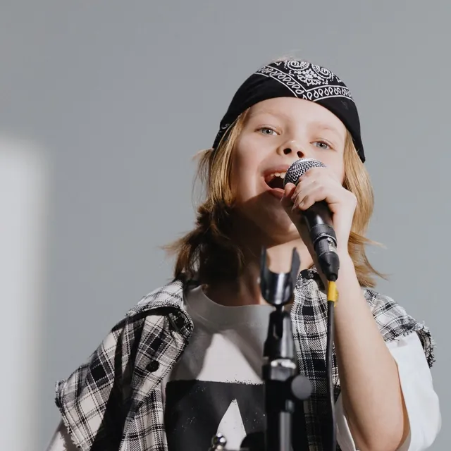 Kid in a plaid shirt singing up into a microphone