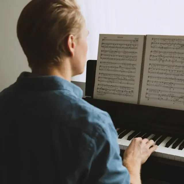 Man playing an upright piano from an open book of sheet music