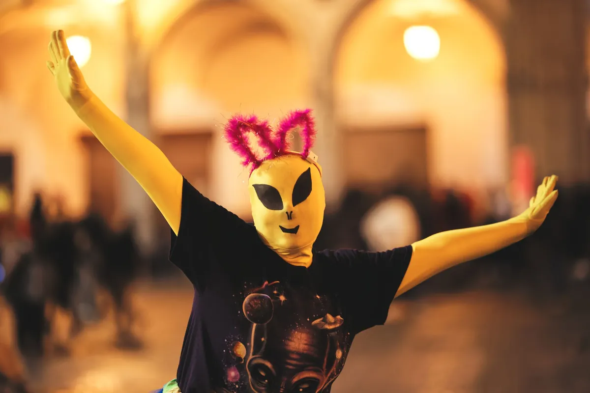 Person in a yellow alien mask with pink antennae dancing at a night party