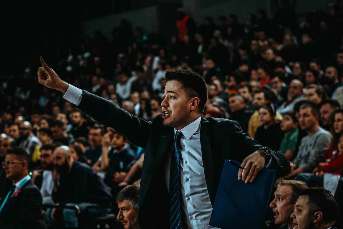 Man in a suit pointing and shouting from the stands of a packed arena
