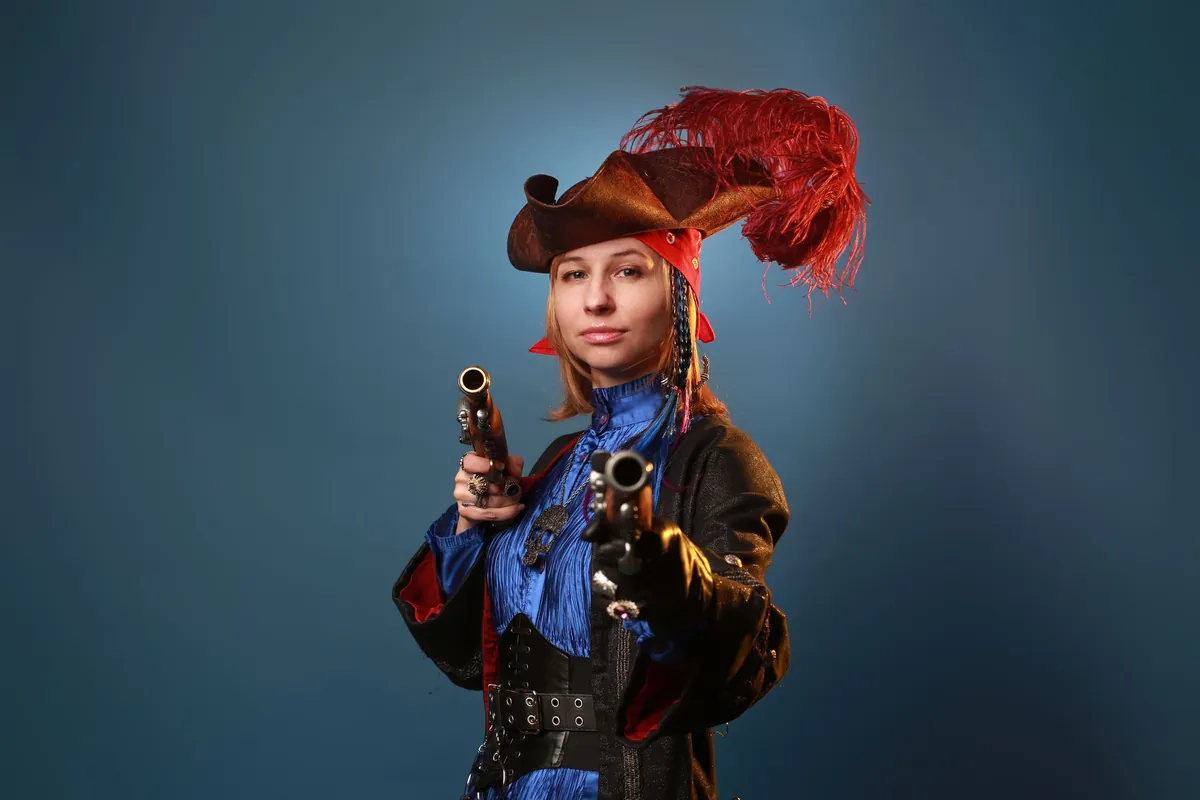 Woman in a homemade pirate costume with a red feathered hat, posing on a blue backdrop