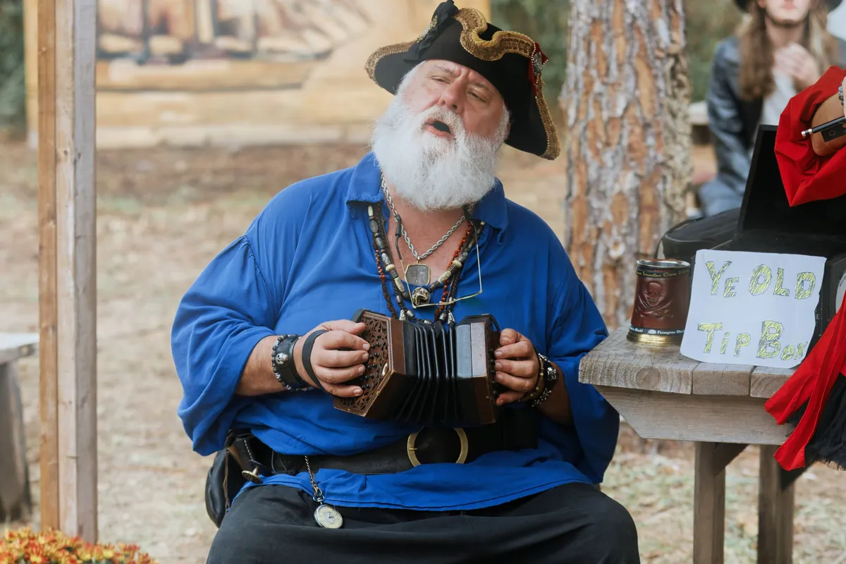 White-bearded man dressed as a pirate laughing as he plays a concertina