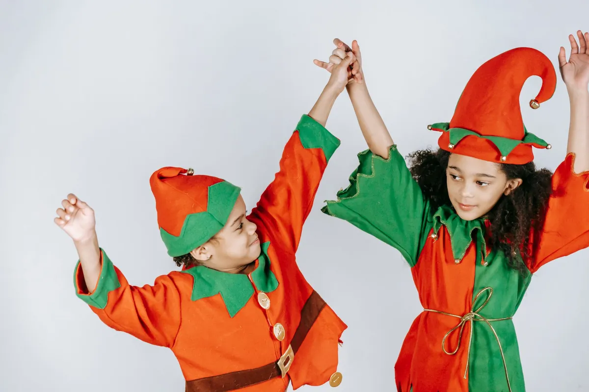 Two kids in Christmas elf costumes dancing with their arms in the air