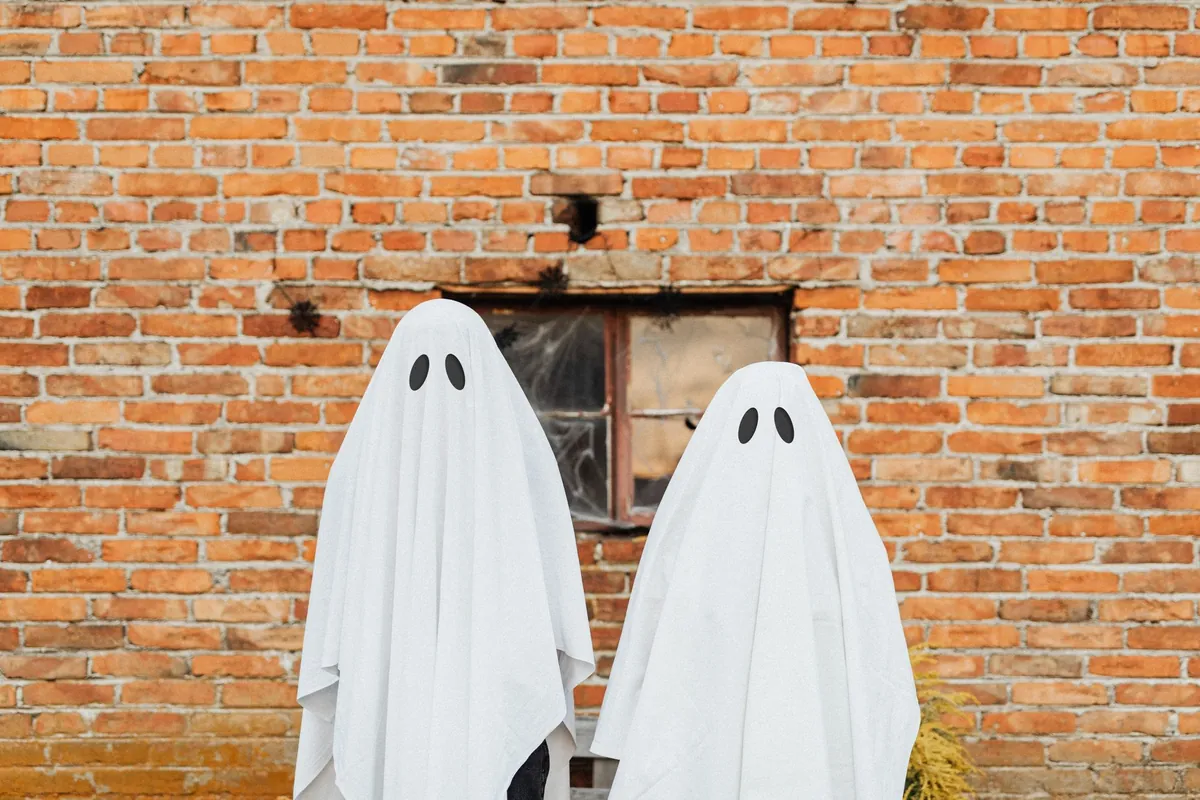 Two people in white ghost sheets standing against a brick wall