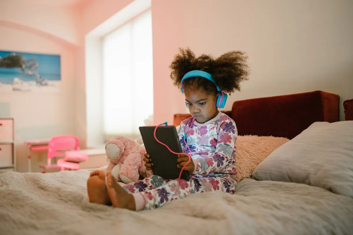 Girl in blue headphones sitting on her bed with a tablet