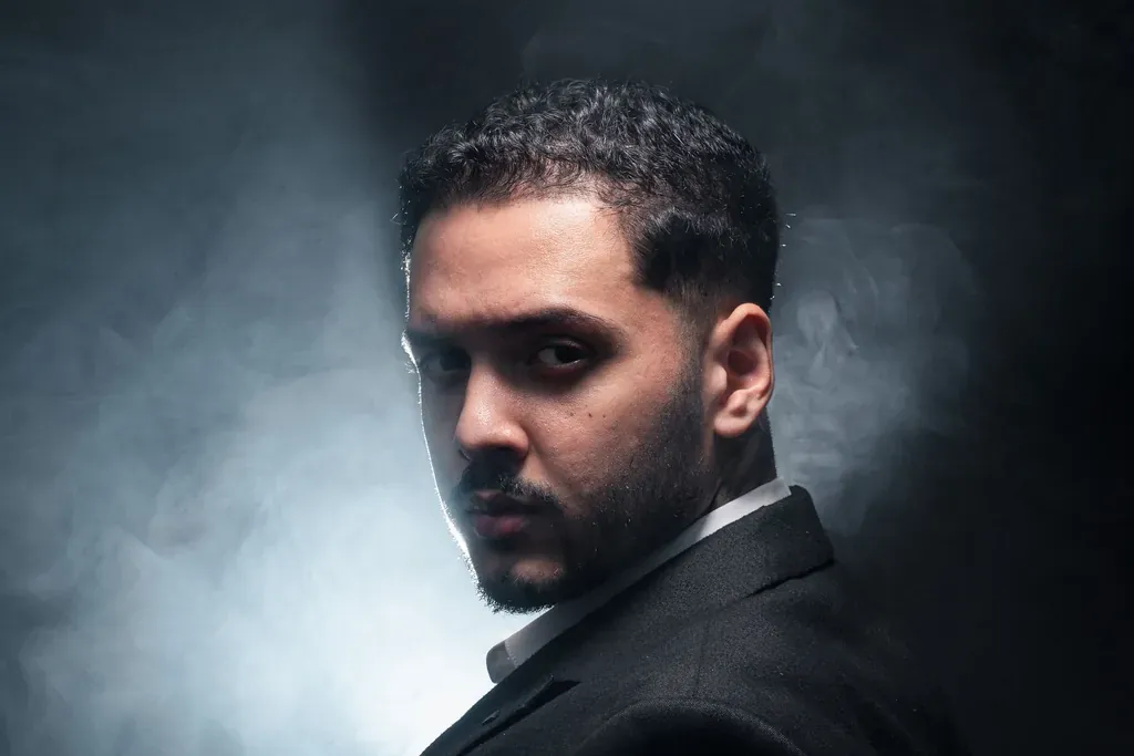 Man in a black suit looking back through smoke and backlight, like a movie trailer hero