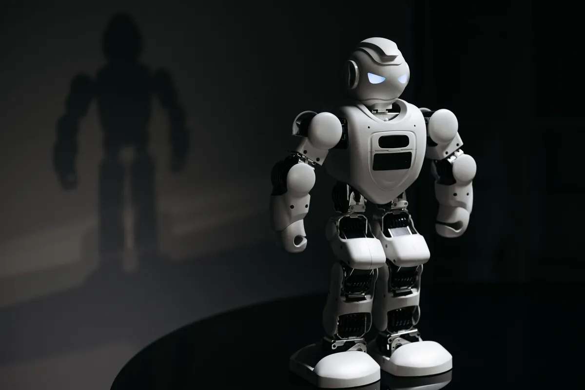 Toy humanoid robot standing in a spotlight with its shadow on the wall