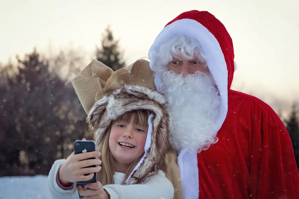Girl in a furry hat taking a selfie with Santa Claus outdoors in winter