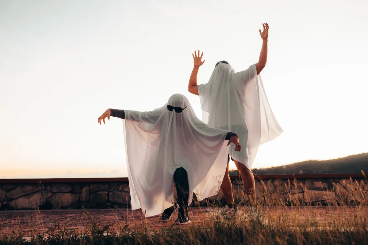 Two people in white ghost sheets dancing in a field at dusk