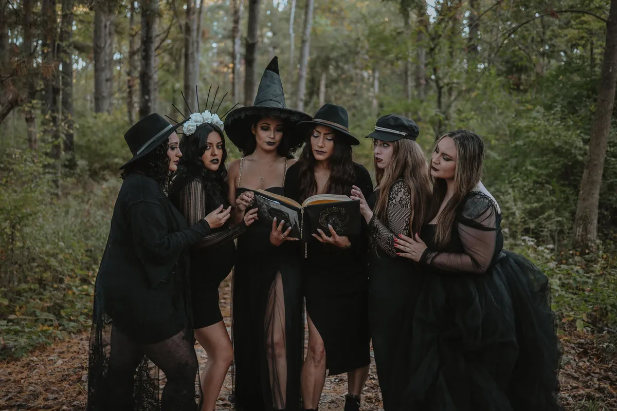 Group of women dressed as witches reading a spell book in a dark forest