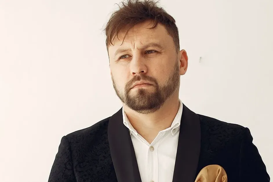 Bearded singer in a black jacket with a pocket square, looking to the side