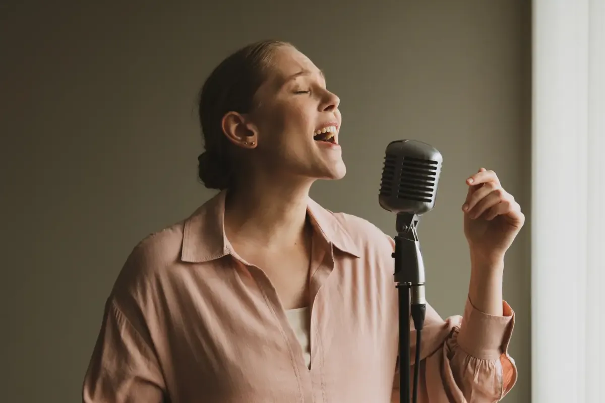 Soprano in a soft pink blouse singing with her eyes closed into a vintage microphone