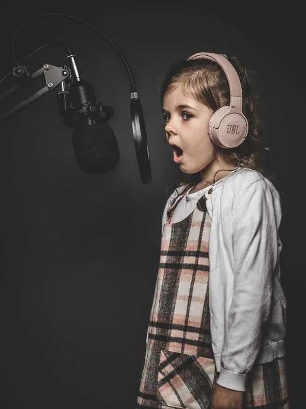 Little girl in big headphones singing at a studio microphone
