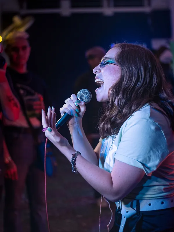 Curly-haired woman singing passionately into a microphone on stage