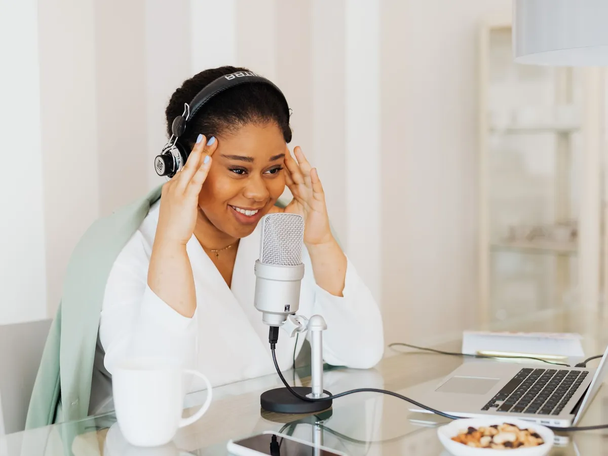 Smiling woman in headphones getting ready at her desk, a USB microphone and laptop in front of her