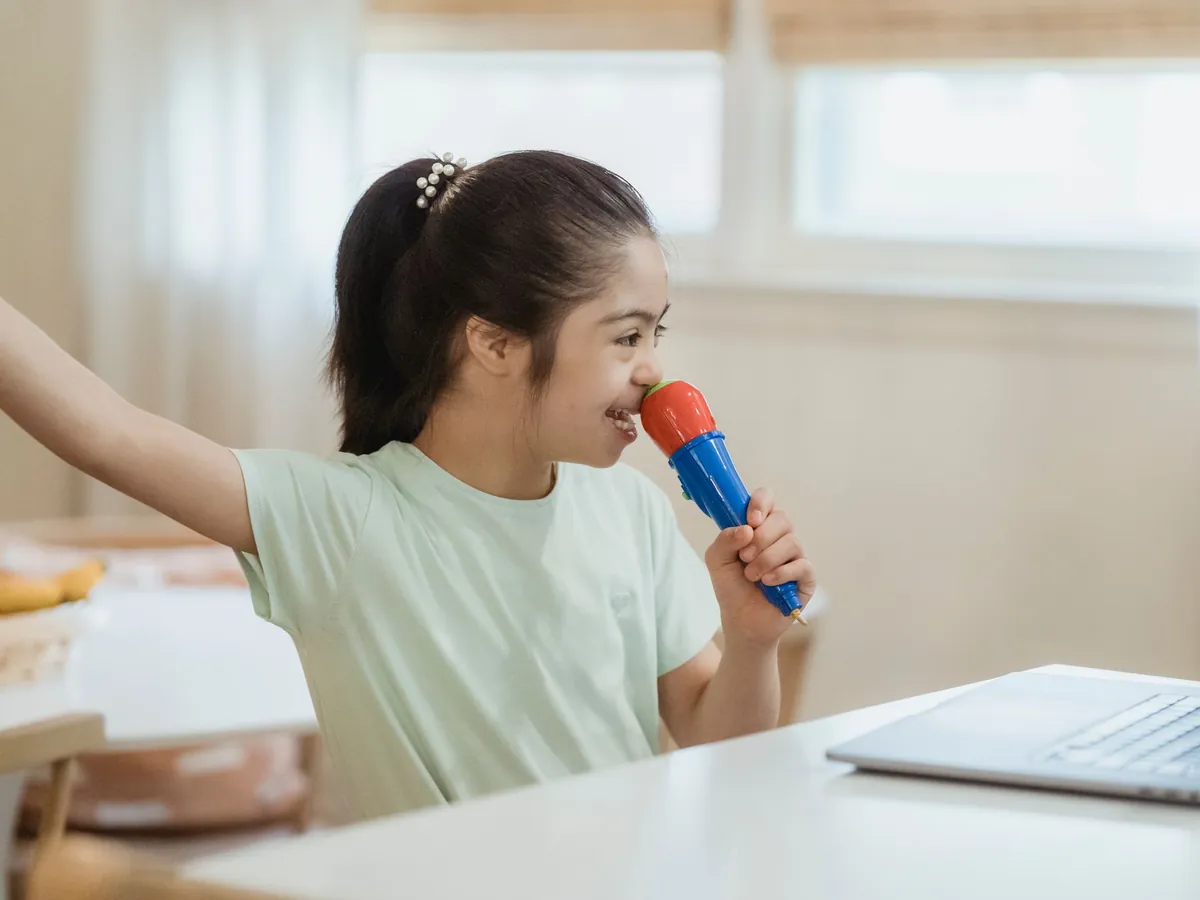 Girl singing into a toy microphone at a table in front of a laptop