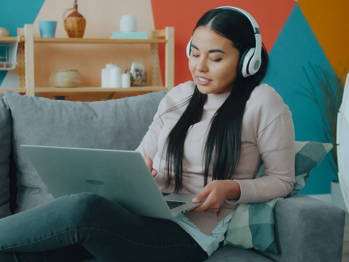 Woman in headphones relaxing on her sofa at home with a laptop on her knees