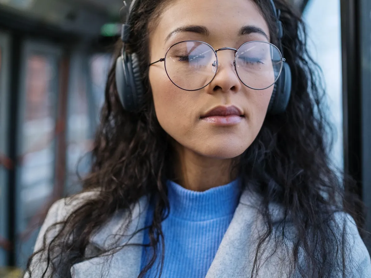 Woman in glasses and headphones listening closely to her own recording