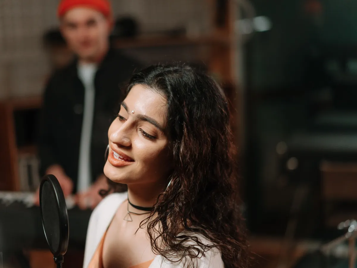 Woman smiling as she sings into a studio microphone
