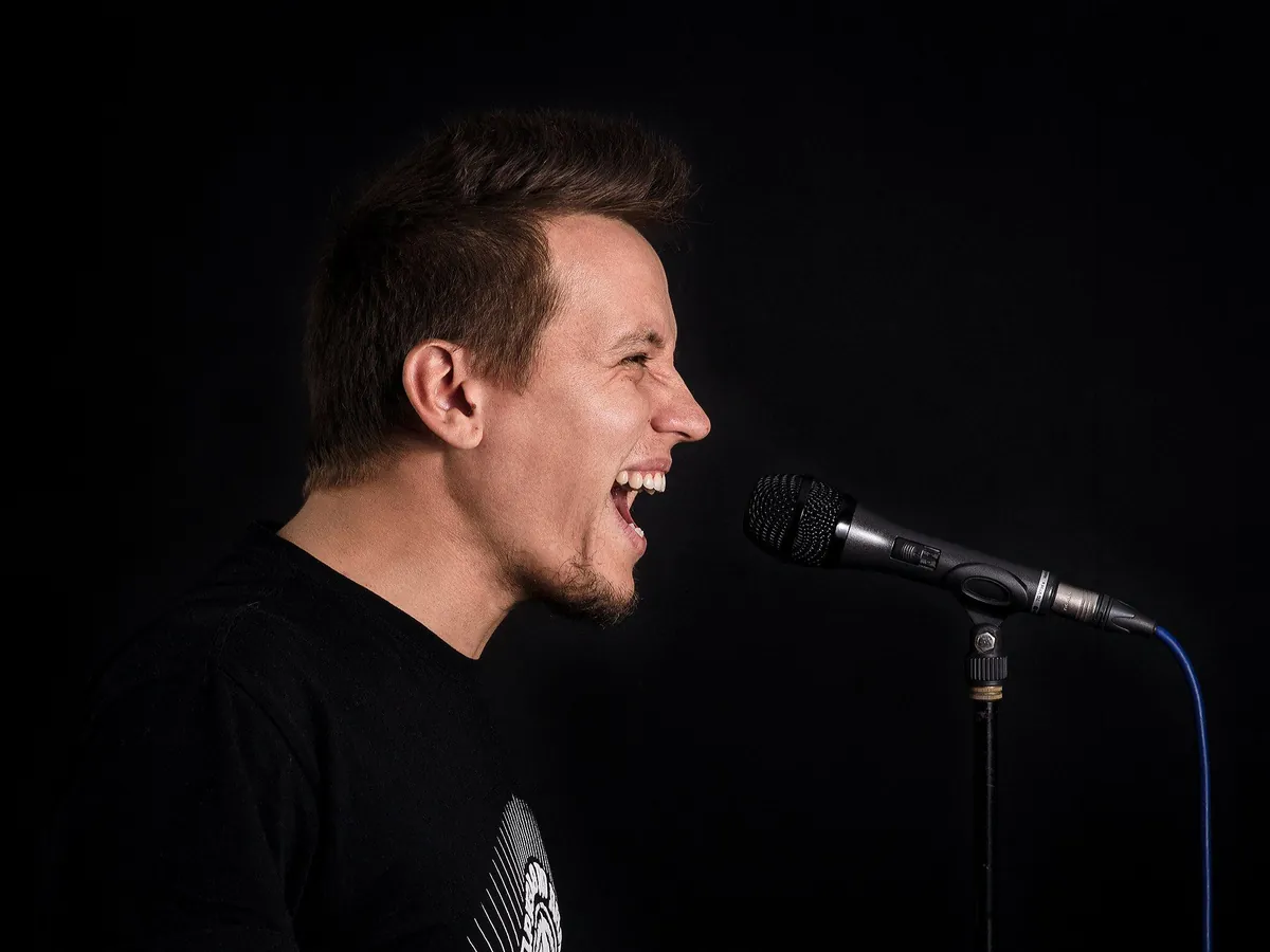 Man in a black T-shirt singing into a microphone on a stand against a black background