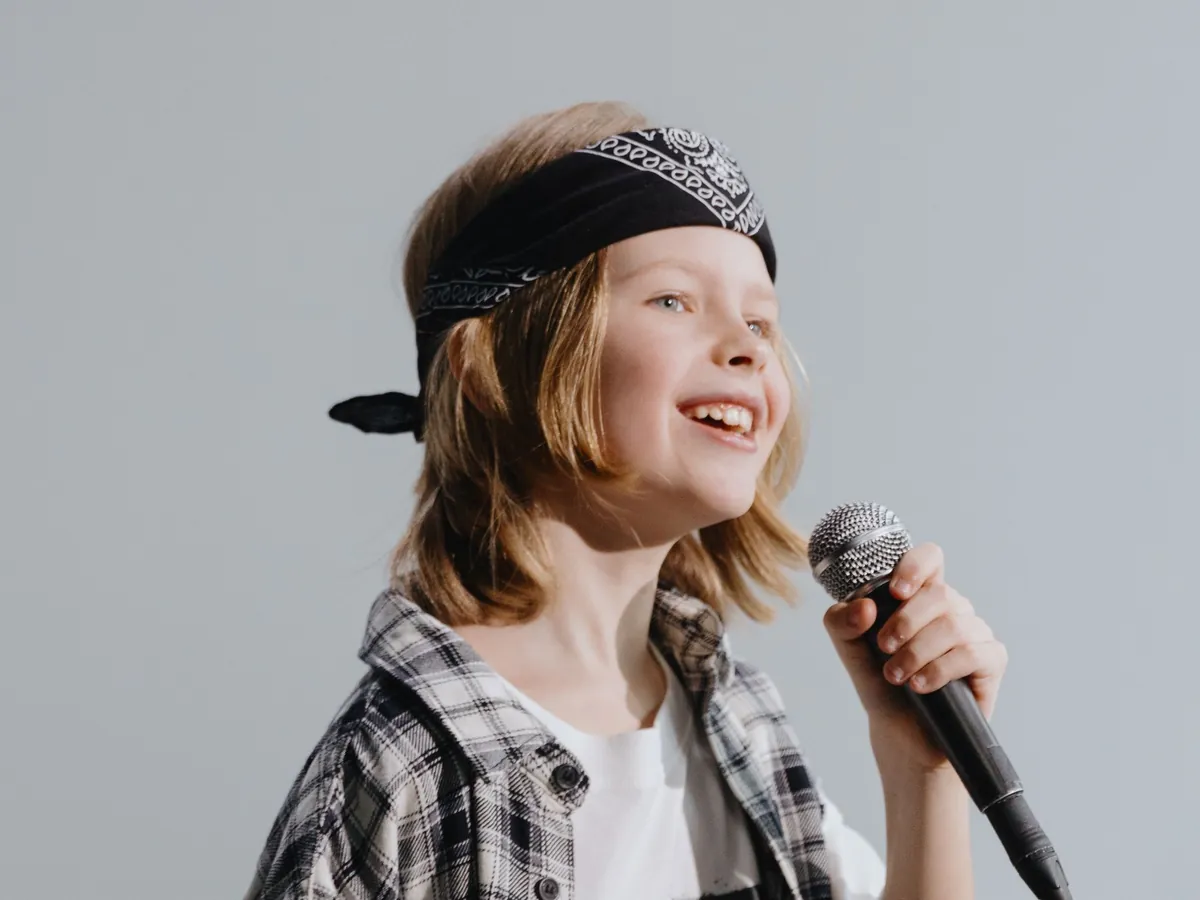 Kid in a plaid shirt and backwards cap singing up into a microphone