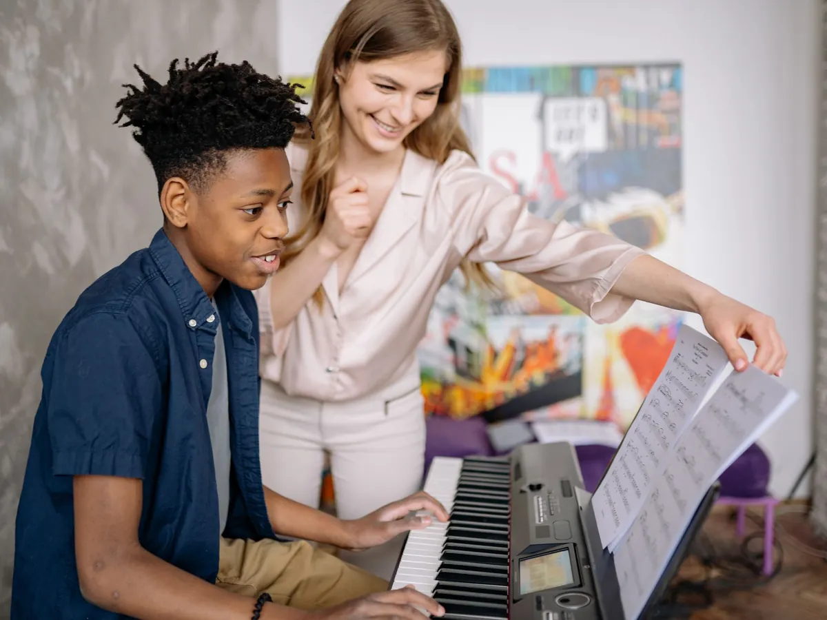 Teacher leaning in to help a boy find the right keys on a digital piano