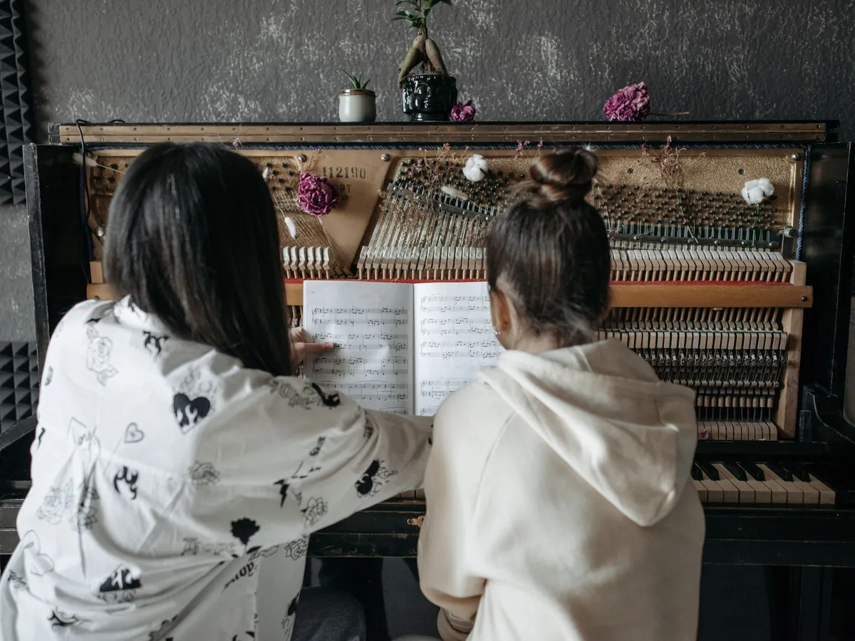Teacher and student reading music together at an upright piano