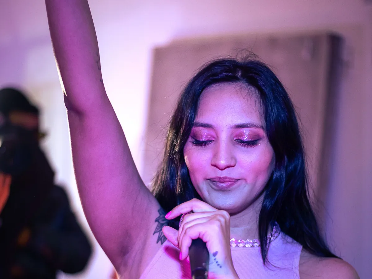 Singer with her arm raised high, hitting a high note under pink stage lights