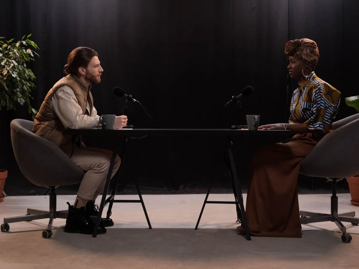 Man and woman talking into microphones across a table in a podcast studio