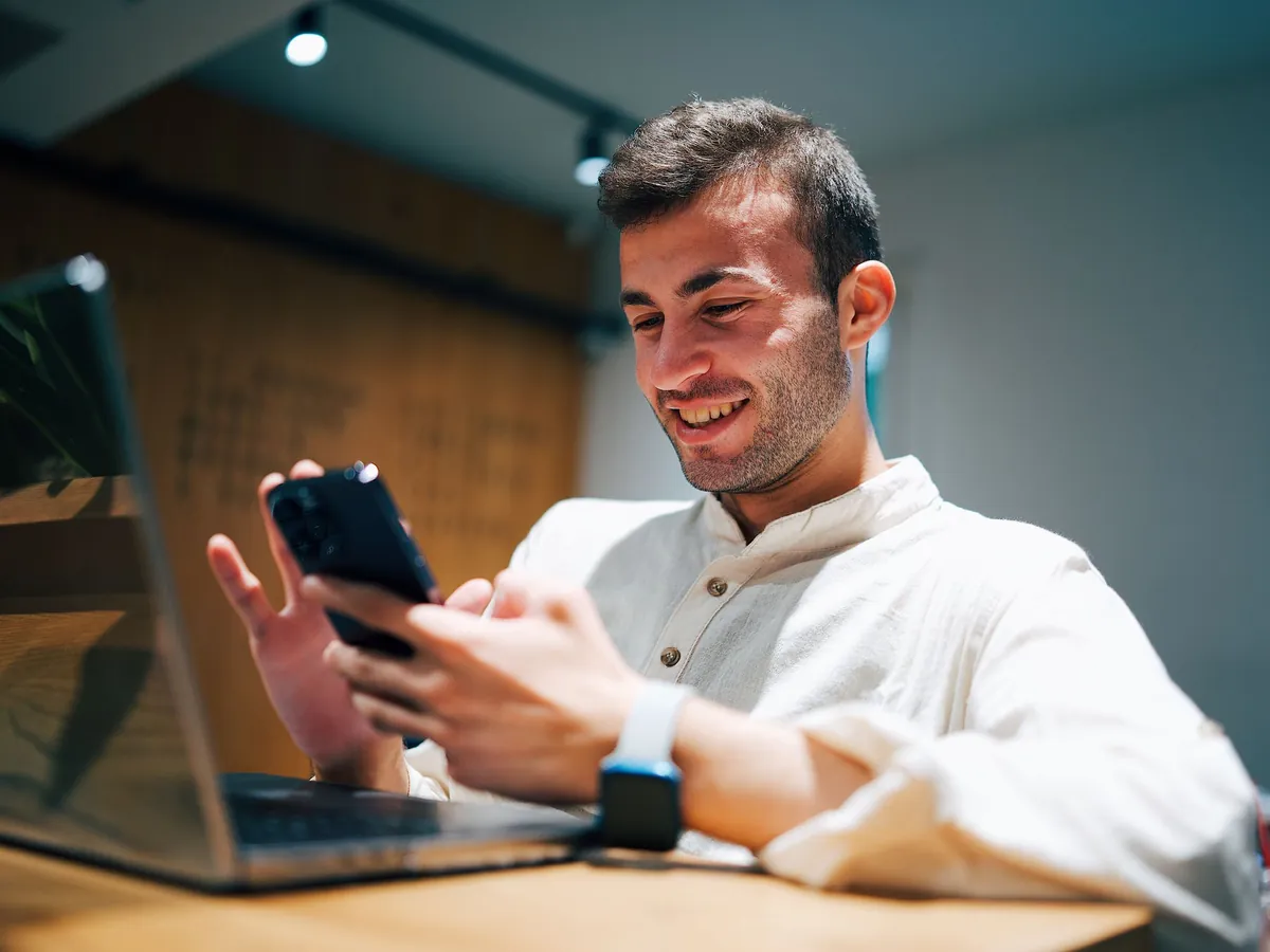 Young man smiling at his phone at a desk, checking his singing score