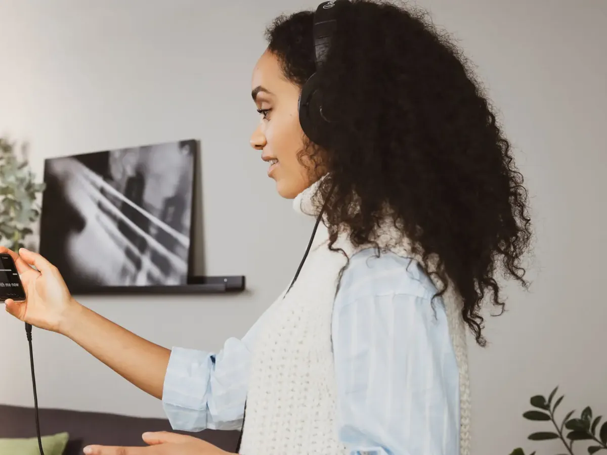 Woman with earphones holding her phone up, singing along in her living room