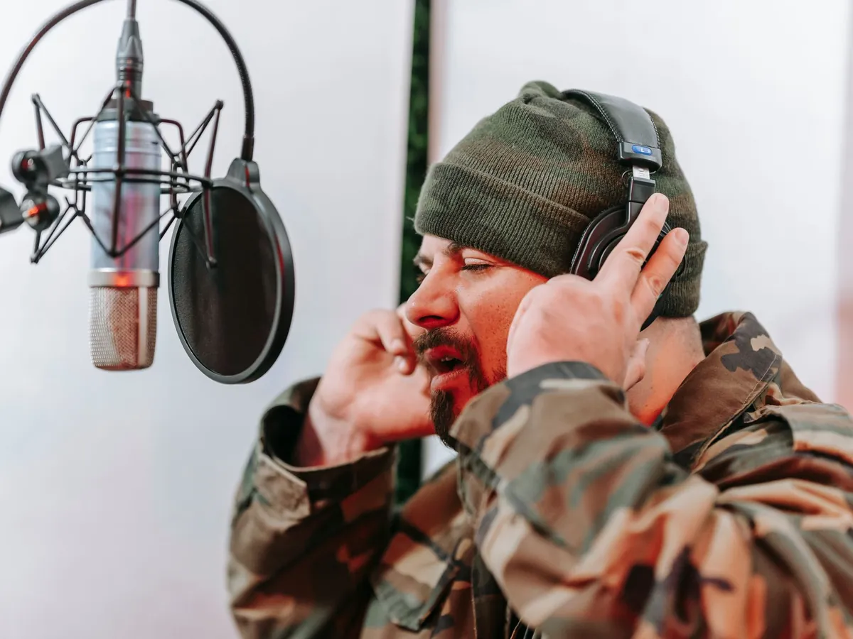 Man in a beanie adjusting his headphones at a studio microphone