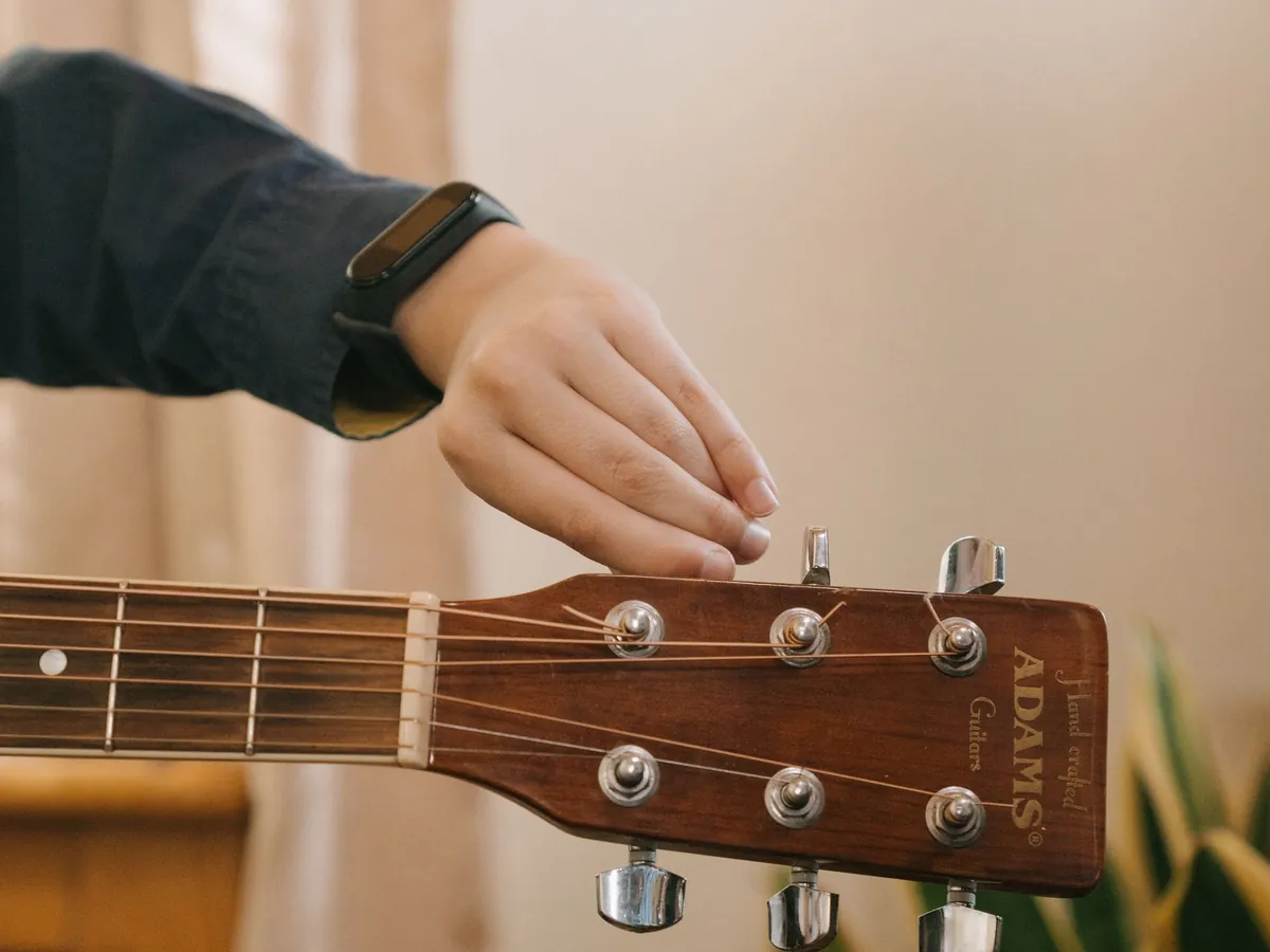 Hand turning a tuning peg on an acoustic guitar headstock