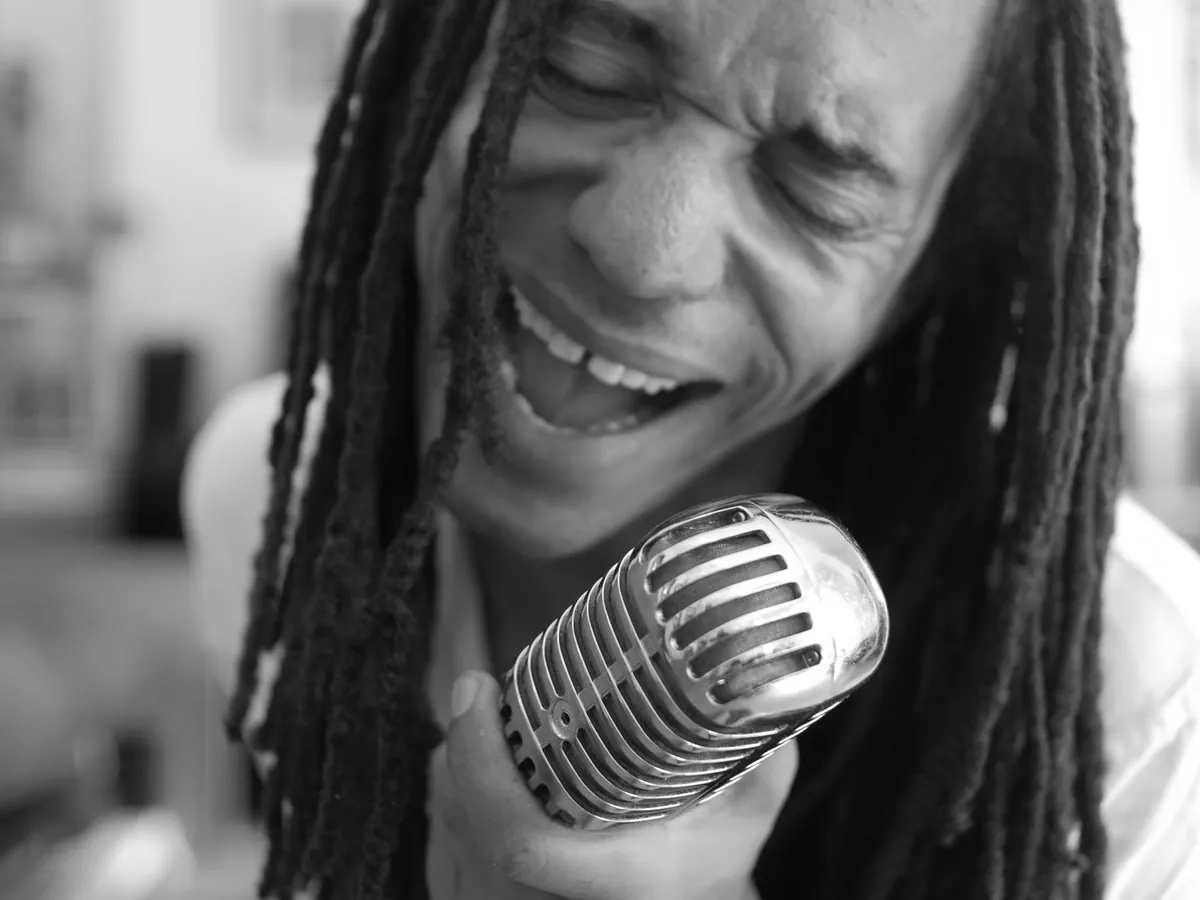 Man with dreadlocks singing into a vintage microphone, in black and white