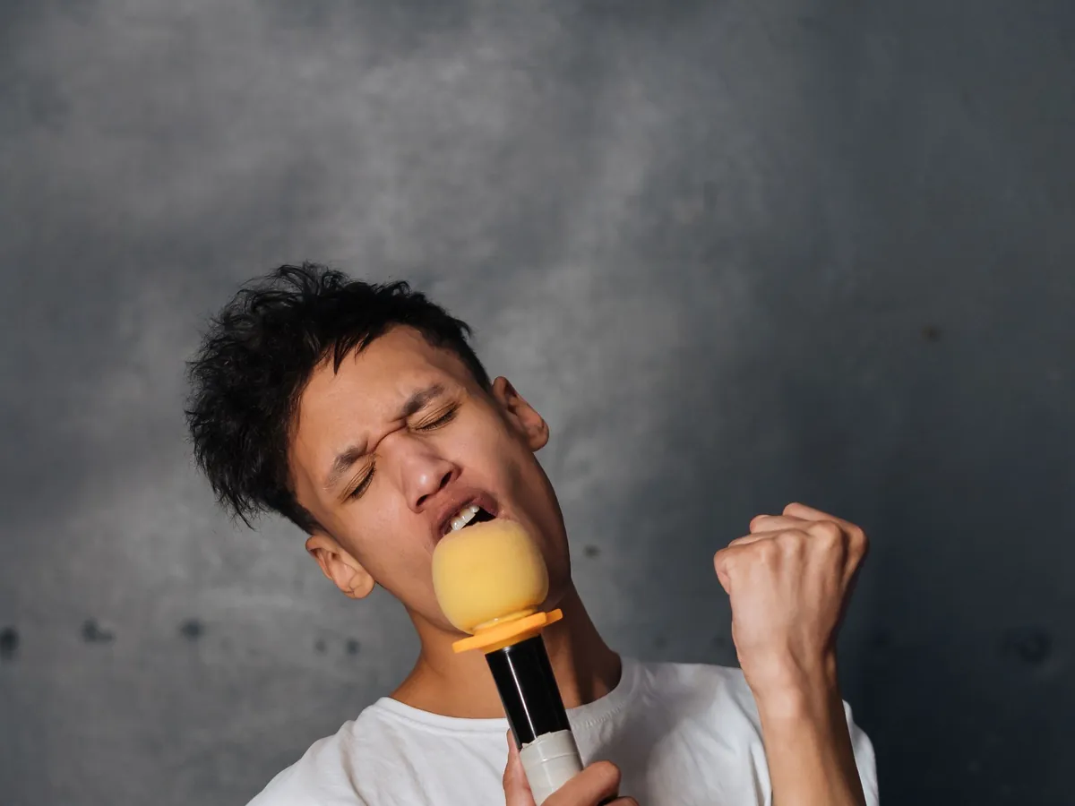 Young man singing a high note into a yellow microphone with his eyes closed