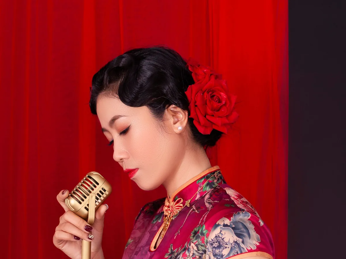 Singer in a floral qipao singing into a gold vintage microphone in front of a red curtain