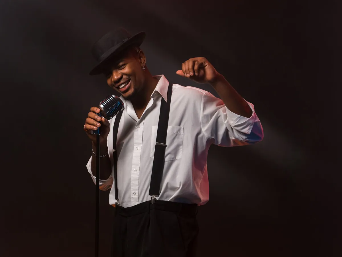 Singer in a hat and suspenders singing into a microphone on a dark stage